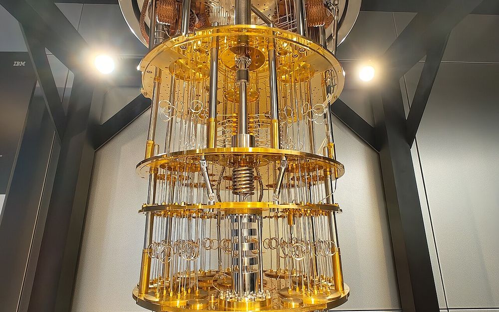 A gold-plated stack of round plates joined by rods and coiled wiring hangs from a steel housing: the cooling assembly of an IBM quantum computer.
